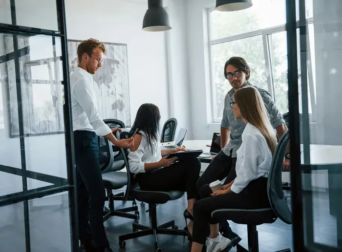 Group of young professionals having a meeting in a bright modern office with glass walls and laptops